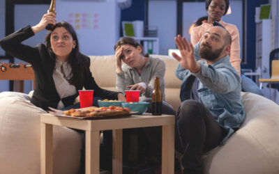 Team of multi ethnic friends losing tv game on console after work at office. Cheerful diverse group play with joystick while eating snacks pizza chips and drinking beer alcohol from cups